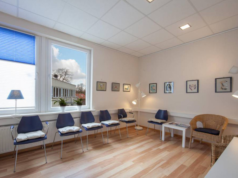 KroMED | Warteraum - Praxis für aesthetische Pigmentierung und Permanent Make-up- Hamburg. Der Warteraum der KroMED-Praxis strahlt eine helle und freundliche Atmosphäre aus, ideal für Kunden und Patienten, die auf Behandlungen wie Permanent Make-up (PMU), Diamant Blading, Brustwarzenpigmentierung und micro Haarpigmentierung warten. Der Raum ist großzügig mit großen Fenstern gestaltet, die viel natürliches Licht einlassen und einen Blick nach draußen ermöglichen. Die Wände sind in einem warmen Beige gehalten, was die Ruhe und Gelassenheit des Raumes unterstreicht. Schwarze Stühle mit schlichten Metallgestellen bieten ausreichend Sitzgelegenheiten entlang der Fensterfront und an der Wand. Einige Pflanzen und dekorative Details, wie Bilder an der Wand, verleihen dem Raum eine angenehme Atmosphäre. Ein kleiner Tisch im Eingangsbereich des Warteraums ist mit verschiedenen Zeitschriften bestückt, die den Patienten die Wartezeit verkürzen. Insgesamt wirkt der Warteraum sauber, aufgeräumt und durchdacht eingerichtet – ein Ort, an dem sich Patienten entspannt auf ihre Behandlung vorbereiten können.